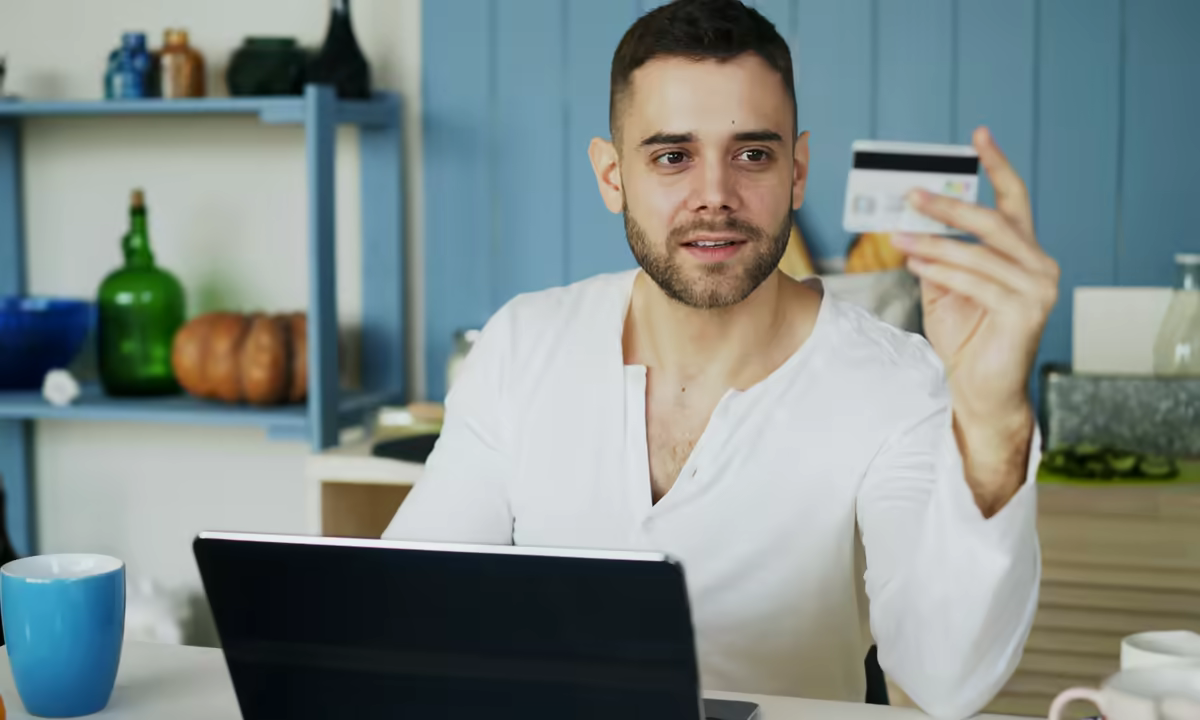 a man holds a payment card in front of a laptop